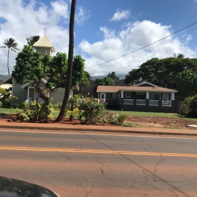 A residential house and a church with a bell tower surrounded by tropical plants under a sunny sky